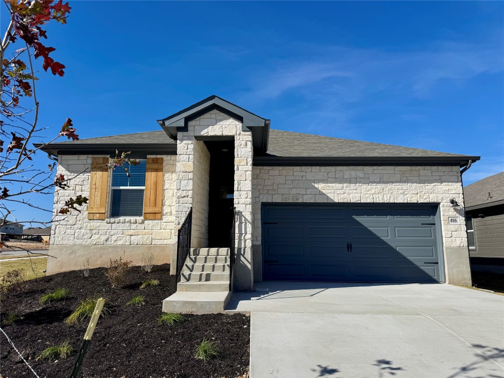 View of front of house with stone siding, concrete driveway, a garage, and a shingled roof