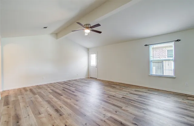an empty room with wooden floor fan and windows