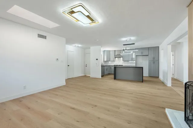a view of an empty room with kitchen and window