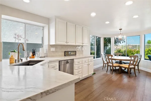 a kitchen with stainless steel appliances granite countertop a stove top oven a sink a dining table and chairs with wooden floor