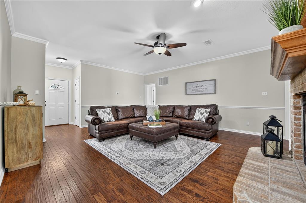 421 Ben Boyd Road Argyle, TX 76226 - Photo 6 of 25 Spacious living area featuring wood-finish flooring, a brick fireplace with a wood mantel, crown molding, and a ceiling fan with integrated lighting