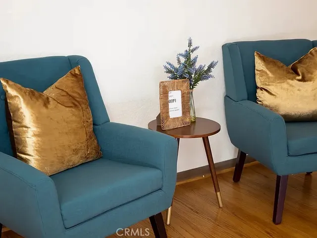a blue chair sitting in a bedroom next to a lamp on dresser and a wooden floor