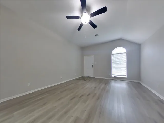 an empty room with wooden floor chandelier fan and windows