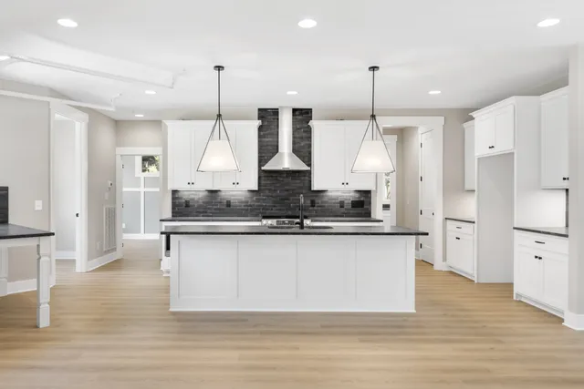 a large kitchen with granite countertop a stove a sink a center island a refrigerator and a wooden floor