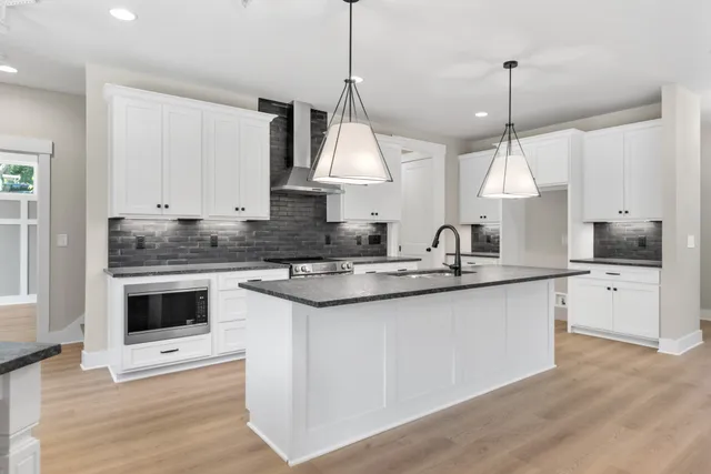 a kitchen with stainless steel appliances granite countertop a sink a stove a refrigerator and white cabinets