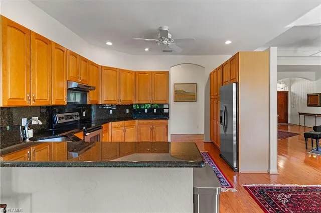 a kitchen with stainless steel appliances granite countertop a refrigerator a stove and a sink with wooden floor