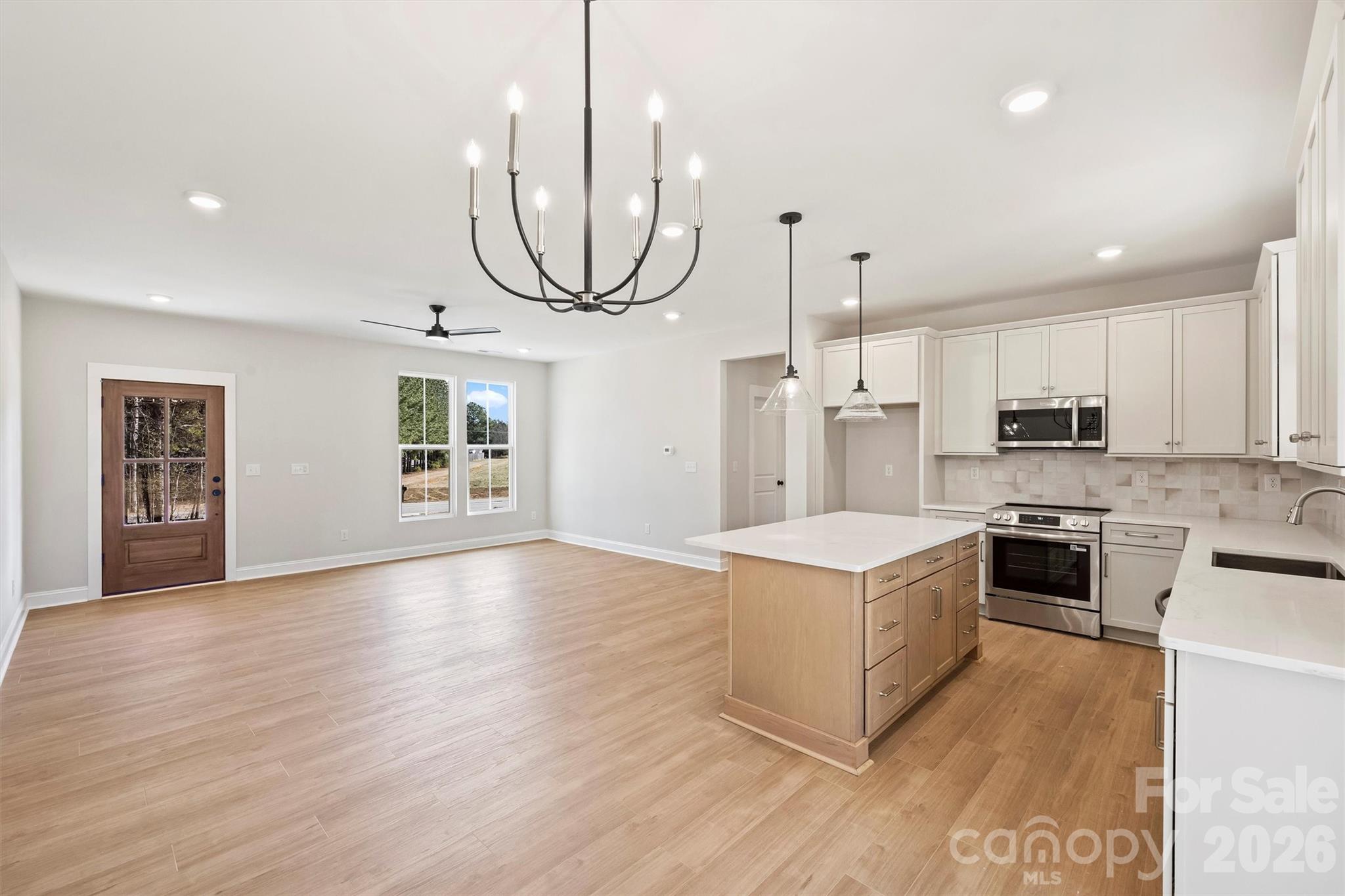 a kitchen with stainless steel appliances granite countertop a stove top oven a sink dishwasher a refrigerator and a dining table with wooden floor