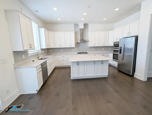 a kitchen with stainless steel appliances a sink a stove a refrigerator cabinets and a window