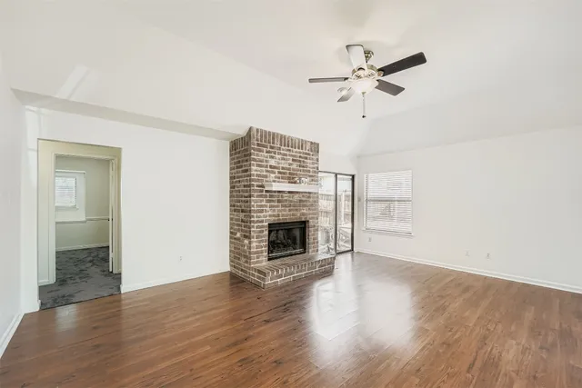 an empty room with wooden floor chandelier fan and windows