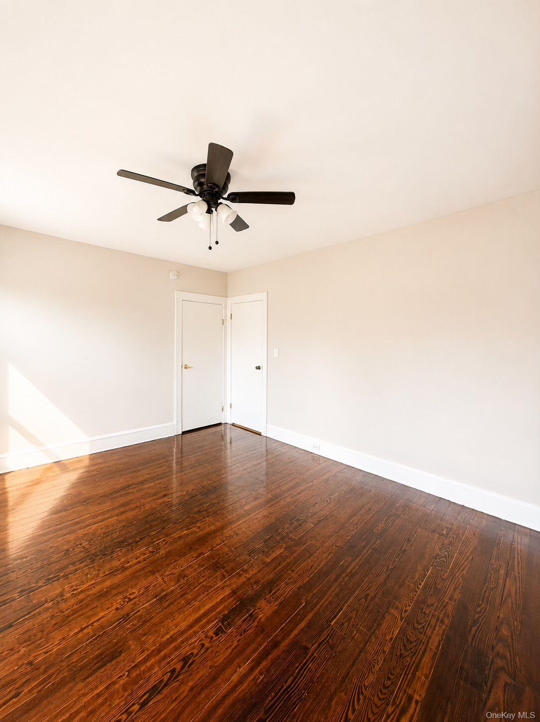 79 Division Street, Unit 3 New Rochelle, NY 10805 - Photo 5 of 17 Spacious room with dark wood-finish flooring, multiple windows, and a ceiling fan with integrated lighting.