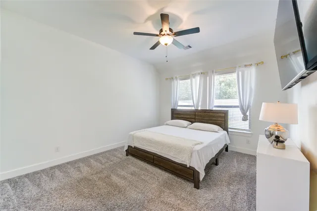 a spacious bedroom with a bed and a flat tv screen on the dresser