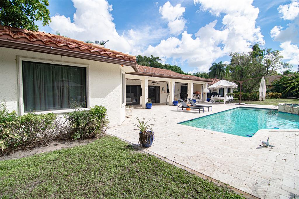 8208 Twin Lake Drive Boca Raton, FL 33496 - Photo 31 of 53 a view of a white house with a swimming pool and a lawn chairs under an umbrella