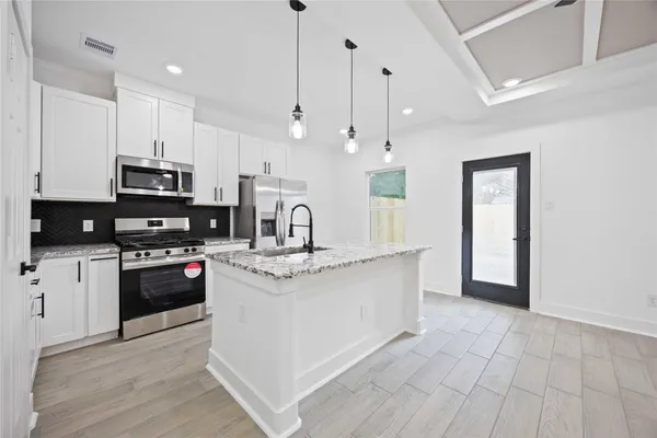 a kitchen with stainless steel appliances kitchen island granite countertop a stove a sink and white cabinets