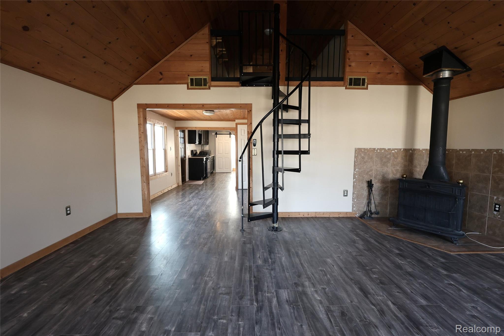 15676 Frazho Road Roseville, MI 48066 - Photo 4 of 20 Open-concept main living area featuring dark wood-finish flooring, a spiral staircase, and a prominent wood-burning stove with a tiled surround