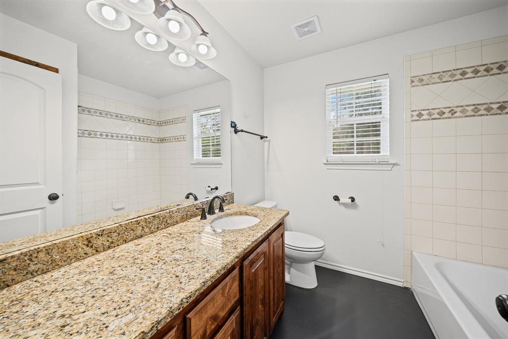 229 Firefly Drive Springtown, TX 76082 - Photo 15 of 33 Bathroom featuring a granite countertop vanity with a single basin, a white porcelain toilet, and a bathtub with white tile surround and decorative accents