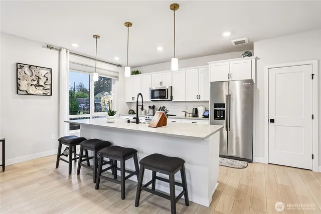 a kitchen with stainless steel appliances a dining table chairs refrigerator and sink