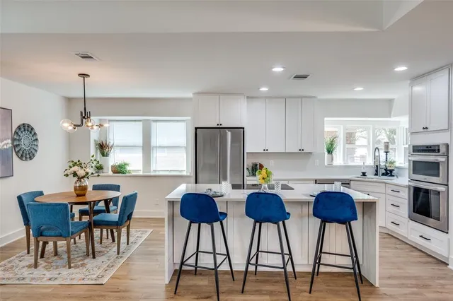 a kitchen with refrigerator a stove a dining table and chairs with wooden floor