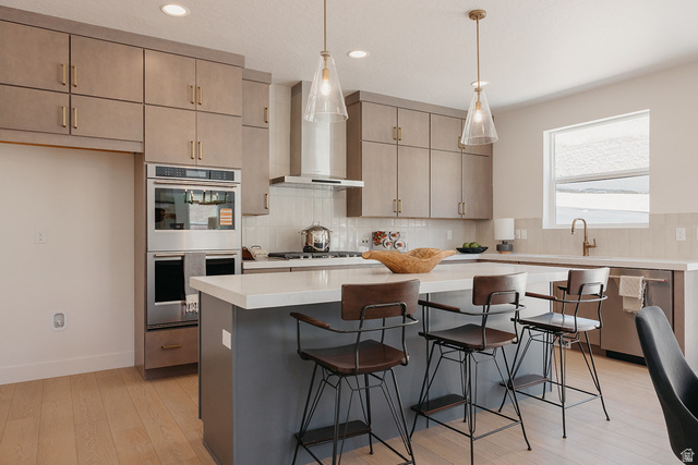 5902 Canyon Rim Road, Unit 620 Lehi, UT 84048 - Photo 4 of 78 Kitchen featuring light wood-finish flooring, a central island with countertop seating, stainless steel appliances, upper and lower cabinetry, and a tile backsplash