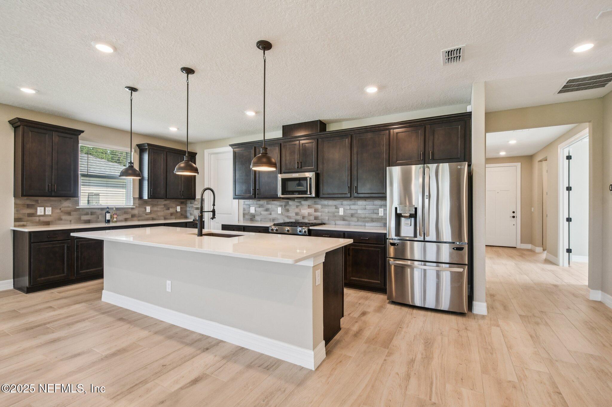 729 Continuum Loop Yulee, FL 32097 - Photo 12 of 31 a kitchen with stainless steel appliances kitchen island granite countertop a refrigerator a stove a sink and a wooden floors