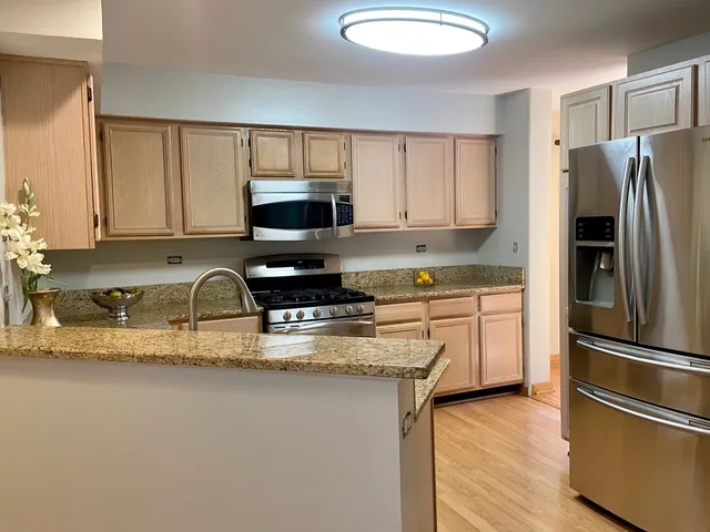 a kitchen with granite countertop a refrigerator a sink a stove a microwave and wooden floor