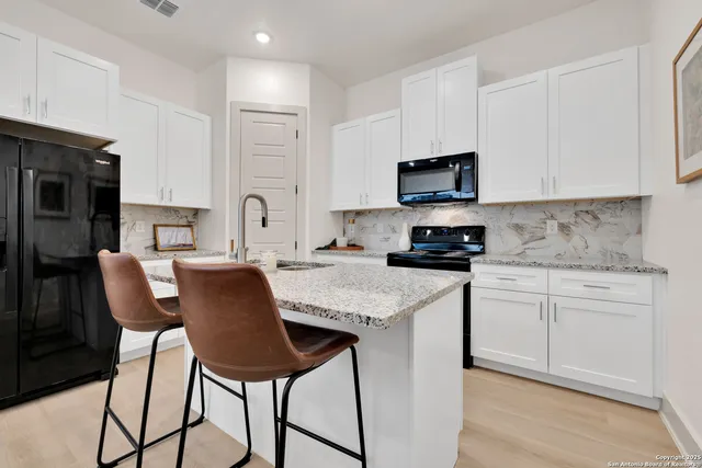 a kitchen with stainless steel appliances granite countertop a stove a sink a refrigerator white cabinets and a microwave