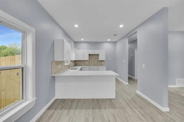 a large white kitchen with wooden floor and a window