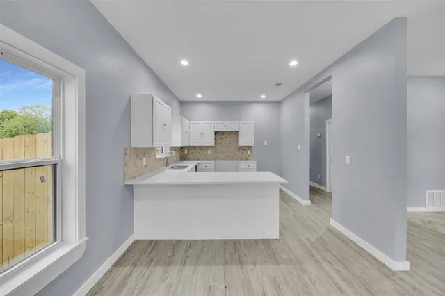 a large white kitchen with wooden floor and a window