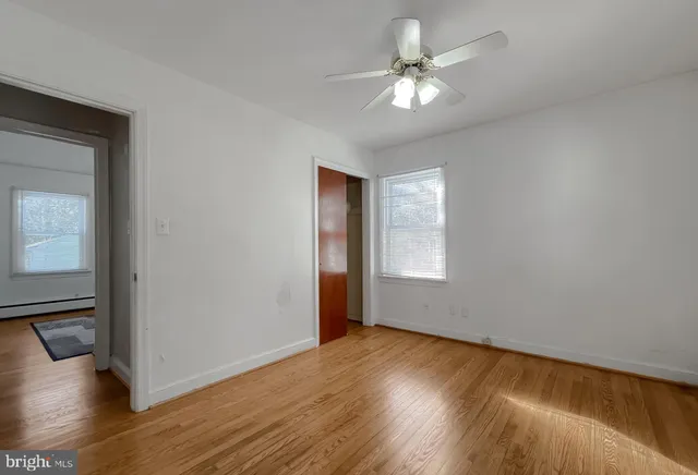a view of an empty room with wooden floor and a ceiling fan