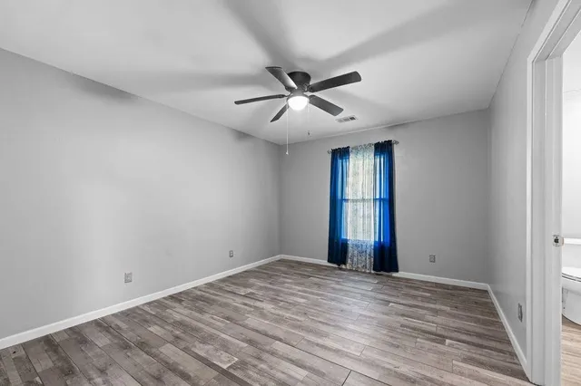 an empty room with wooden floor ceiling fan and windows
