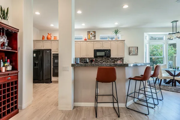 a kitchen with stainless steel appliances kitchen island granite countertop a refrigerator a stove a dining table and chairs with wooden floor