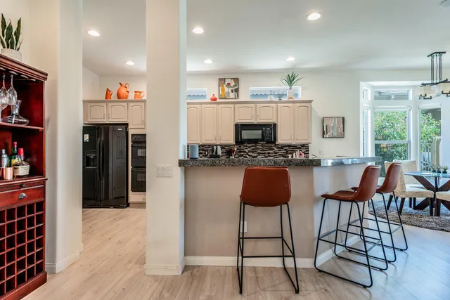 a kitchen with stainless steel appliances kitchen island granite countertop a refrigerator a stove a dining table and chairs with wooden floor