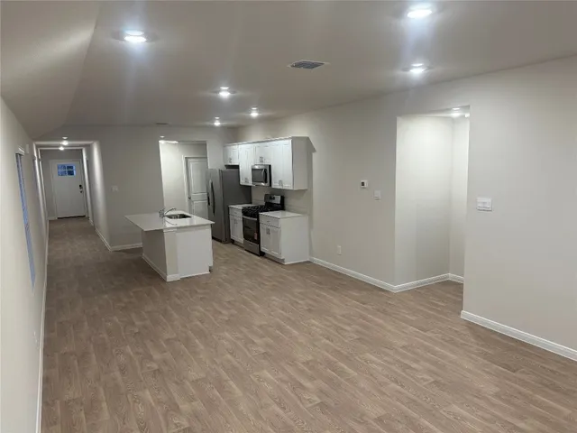 an empty room with wooden floor and stainless steel appliances