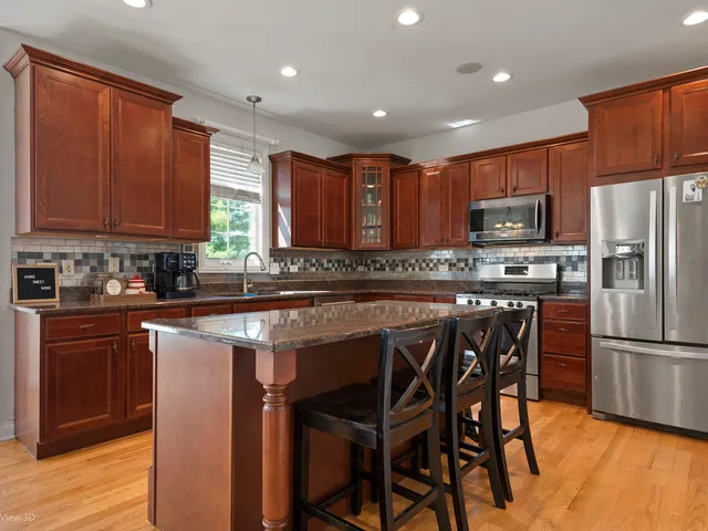 a kitchen with stainless steel appliances granite countertop a stove a refrigerator a sink a dining table and chairs