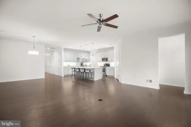 a view of a livingroom with kitchen appliances and a ceiling fan