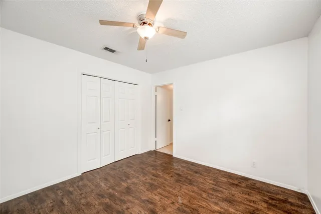 an empty room with a chandelier fan and wooden floor