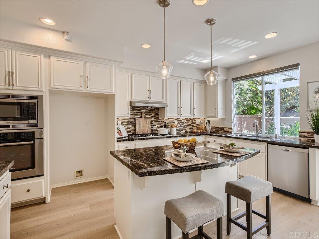 6562 Windflower Drive Carlsbad, CA 92011 - Photo 8 of 28 a kitchen with a sink a stove a refrigerator and white cabinets with wooden floor