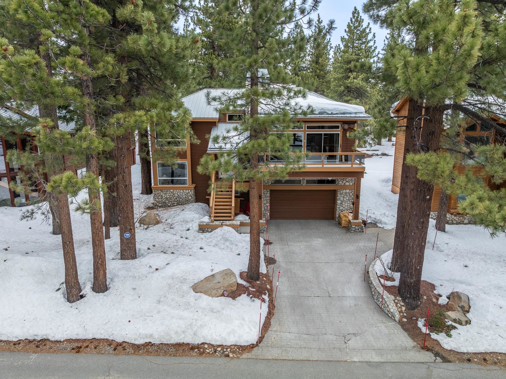 View of front of home featuring a deck, stone siding, a garage, and driveway