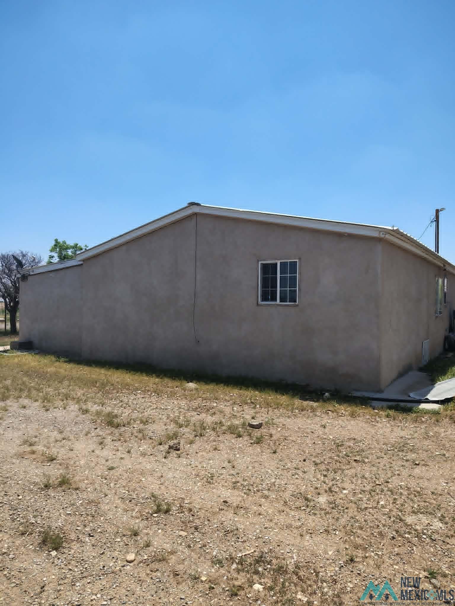 58 Fisk Road Dexter, NM 88230 - Photo 37 of 46 Stucco exterior with a single-pane window and a gravel-and-grass foreground