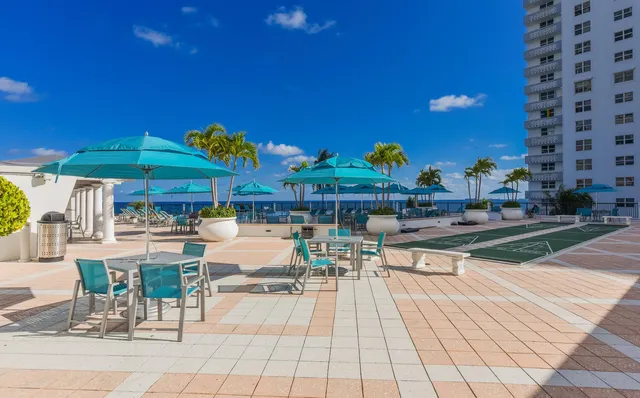 a view of a patio with dining table and chairs under an umbrella with a barbeque grill and plants