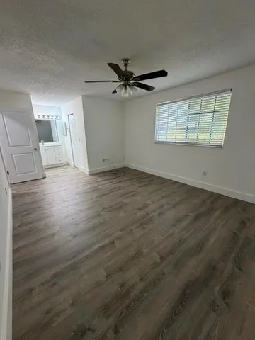 an empty room with wooden floor ceiling fan and windows