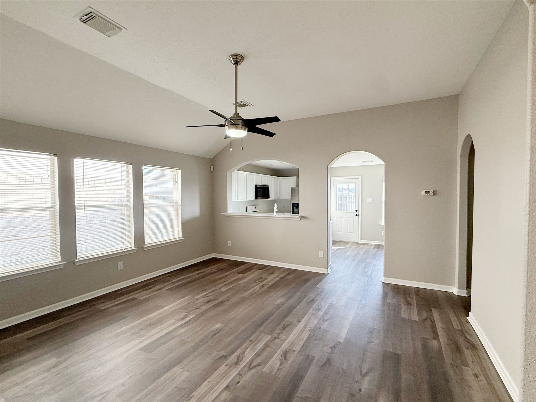 13210 Barton Meadow Lane Rosharon, TX 77583 - Photo 3 of 21 This spacious living area features large windows for natural light, a ceiling fan, and modern wood flooring. It opens to a kitchen with a serving hatch and an arched doorway leading to additional space.