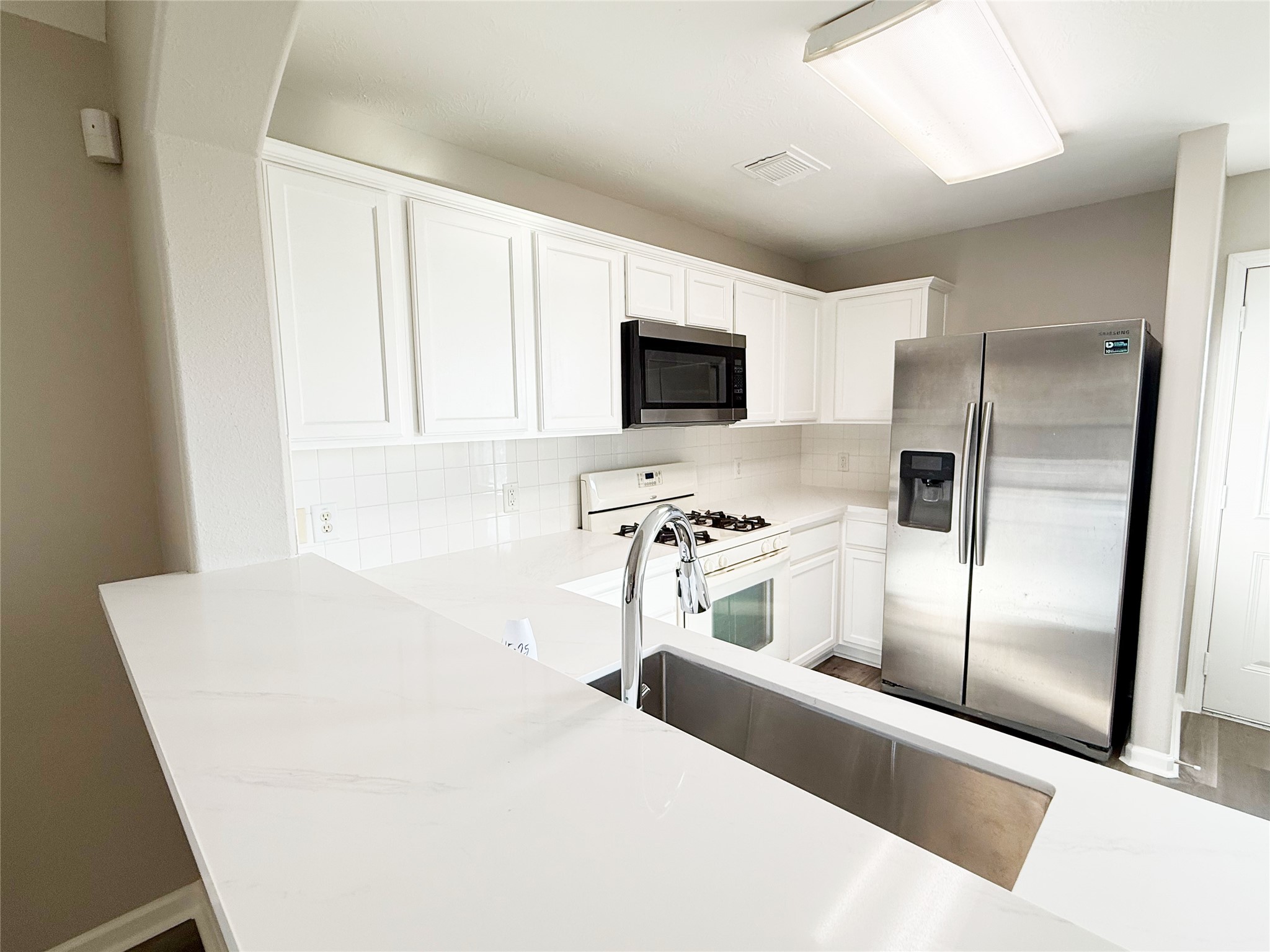 13210 Barton Meadow Lane Rosharon, TX 77583 - Photo 7 of 21 Modern kitchen with sleek white cabinetry, stainless steel appliances, and a spacious countertop. Features a built-in microwave, gas stove, and a double-door fridge. Bright and clean design.