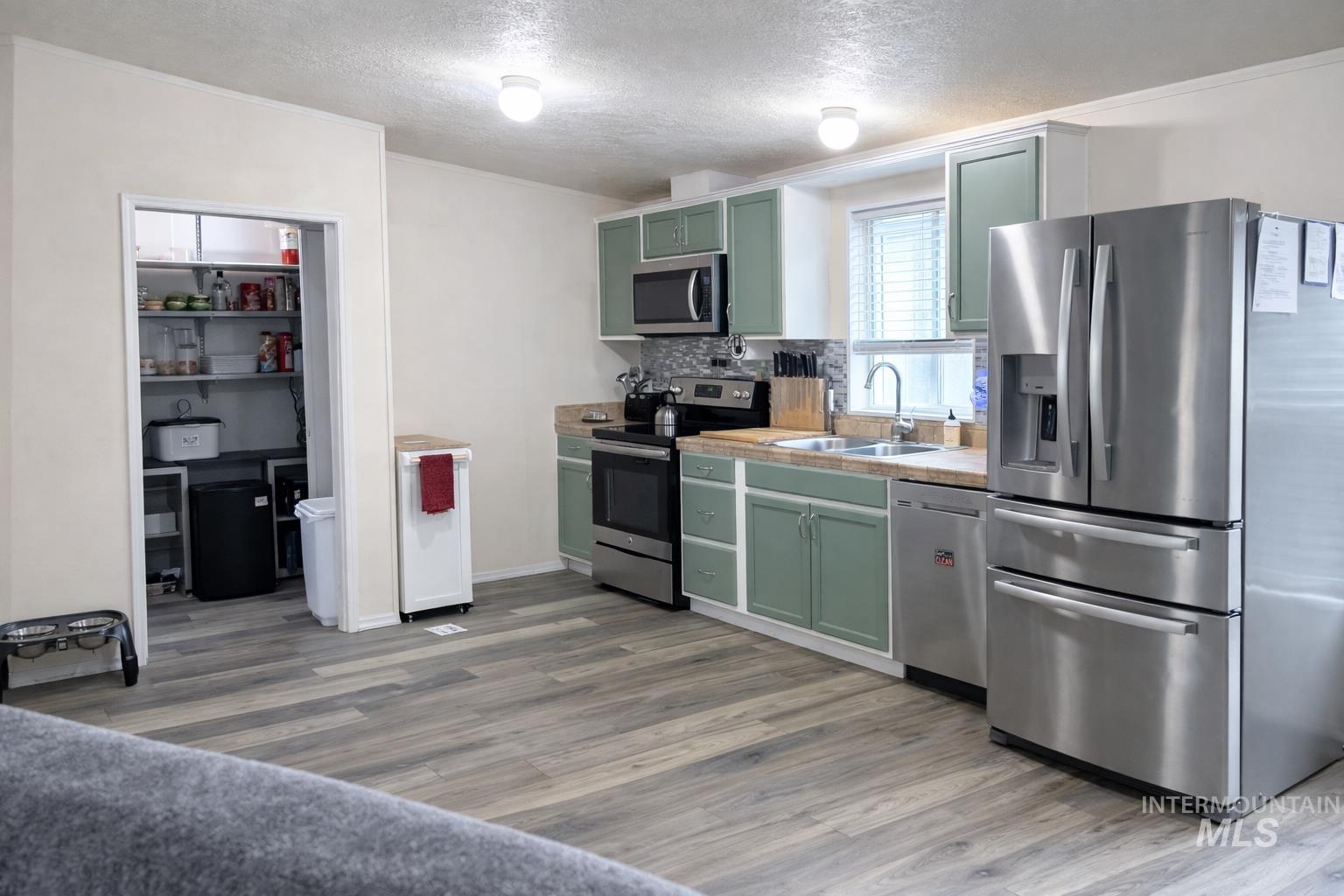 700 East Fairview Avenue, Unit 195 Meridian, ID 83642 - Photo 8 of 19 Kitchen with green cabinetry, stainless steel appliances, a textured ceiling, light countertops, and decorative backsplash