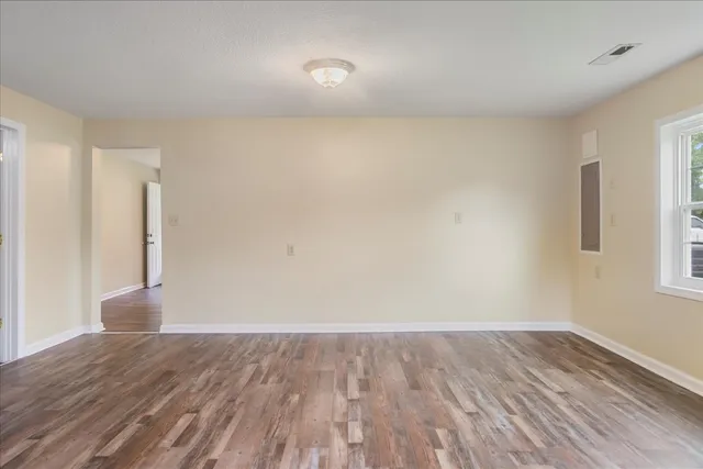 a view of an empty room with wooden floor and a window