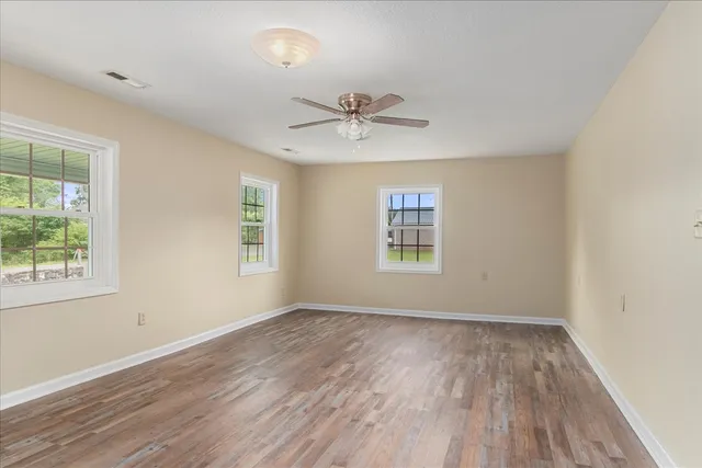 an empty room with wooden floor ceiling fan and windows