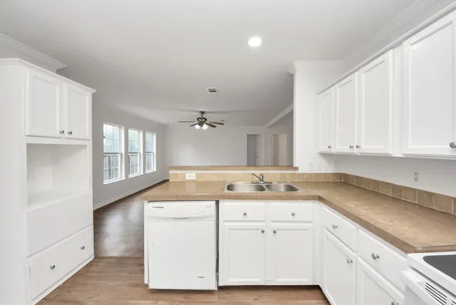 a kitchen with a sink dishwasher and white cabinets with wooden floor