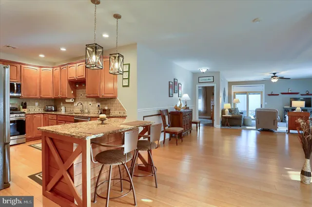 a kitchen with stainless steel appliances granite countertop a stove top oven a refrigerator a sink dishwasher a dining table and chairs with wooden floor