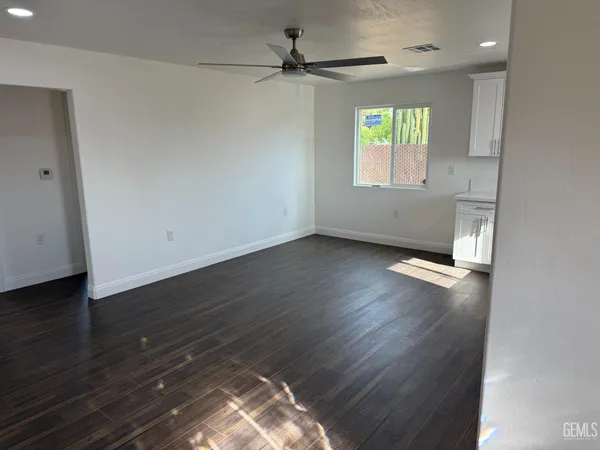 an empty room with wooden floor chandelier fan and windows