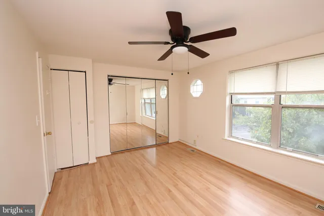 a view of an empty room and window a ceiling fan and wooden floor