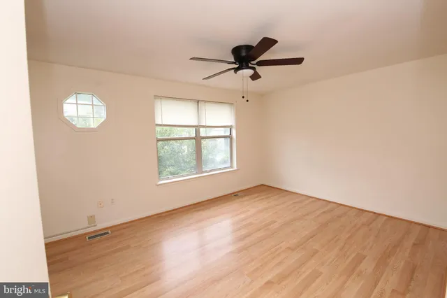 an empty room with wooden floor fan and windows
